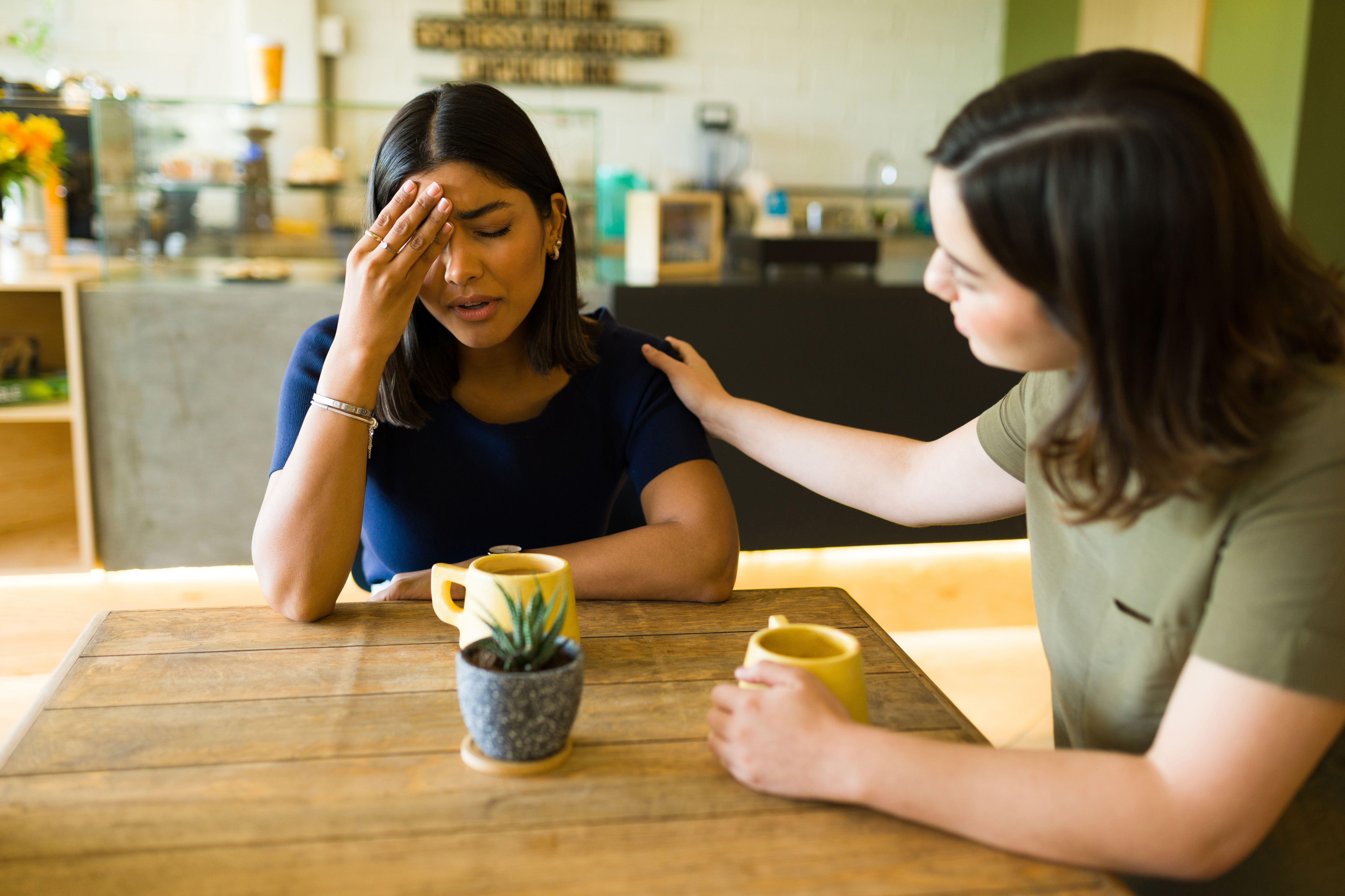 A woman comforting another woman in a coffee shop