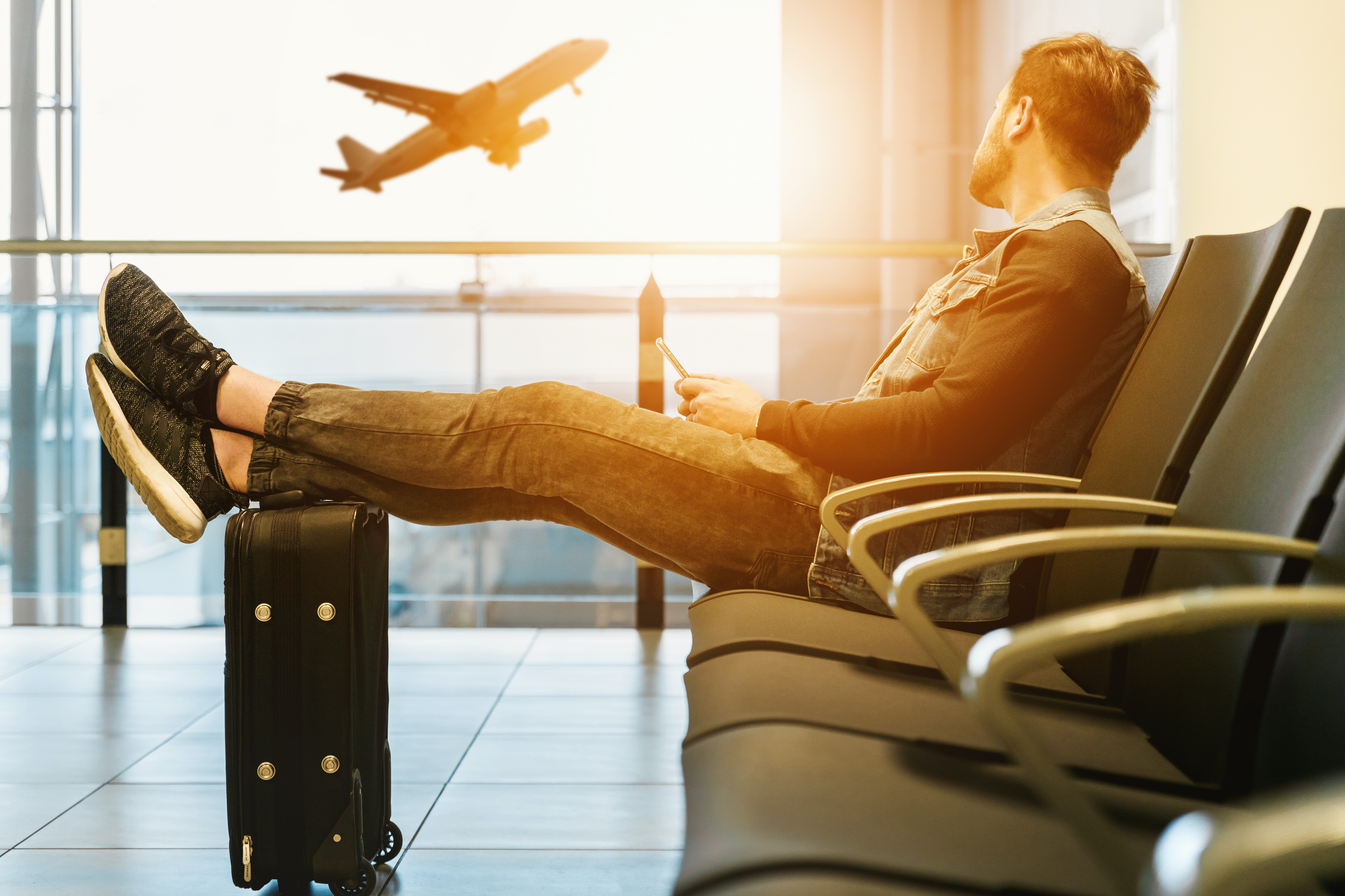 A man sitting with his feet on luggage looking at an airplane at sunset