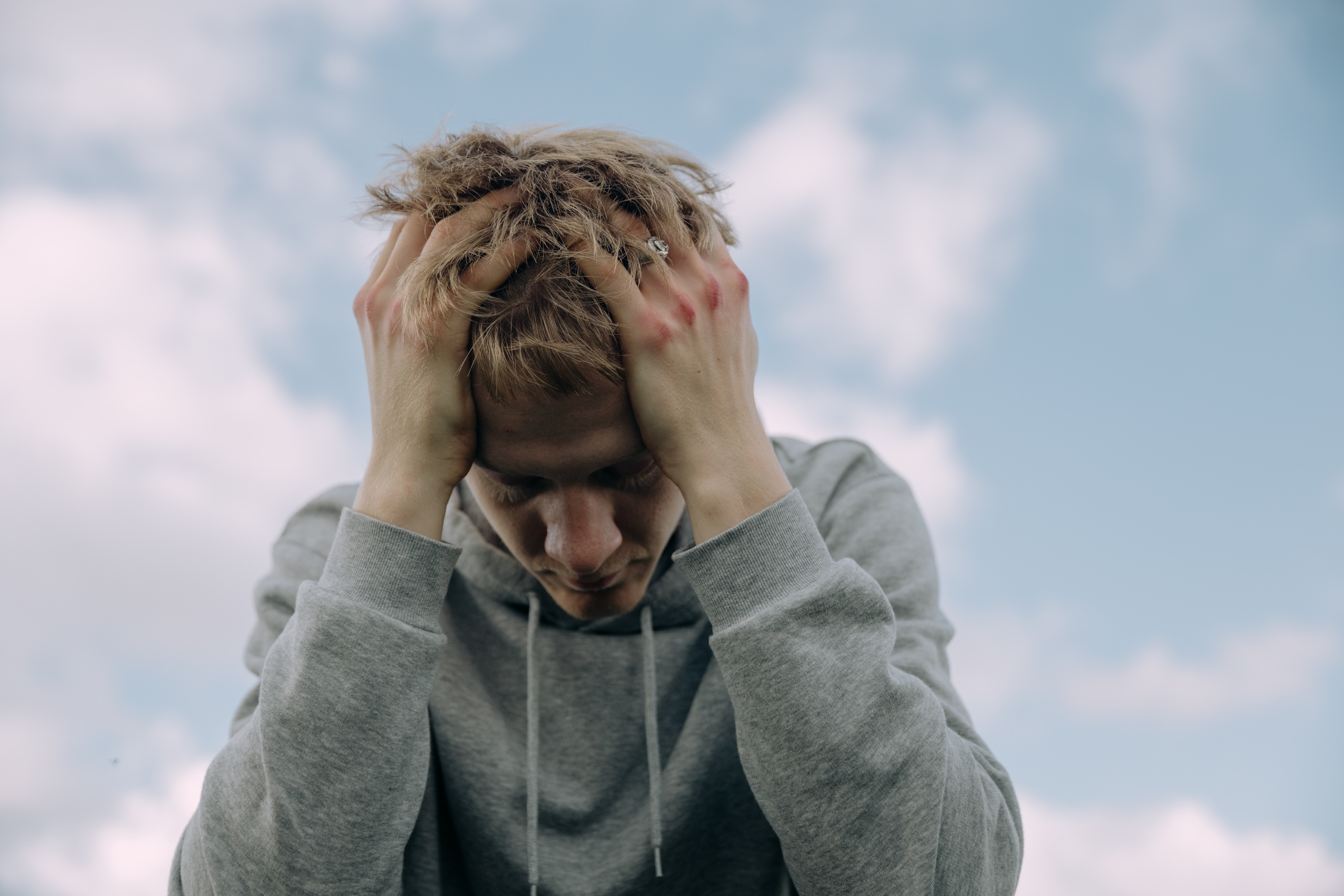 A man in a grey sweatshirt leaning forward and holding his head