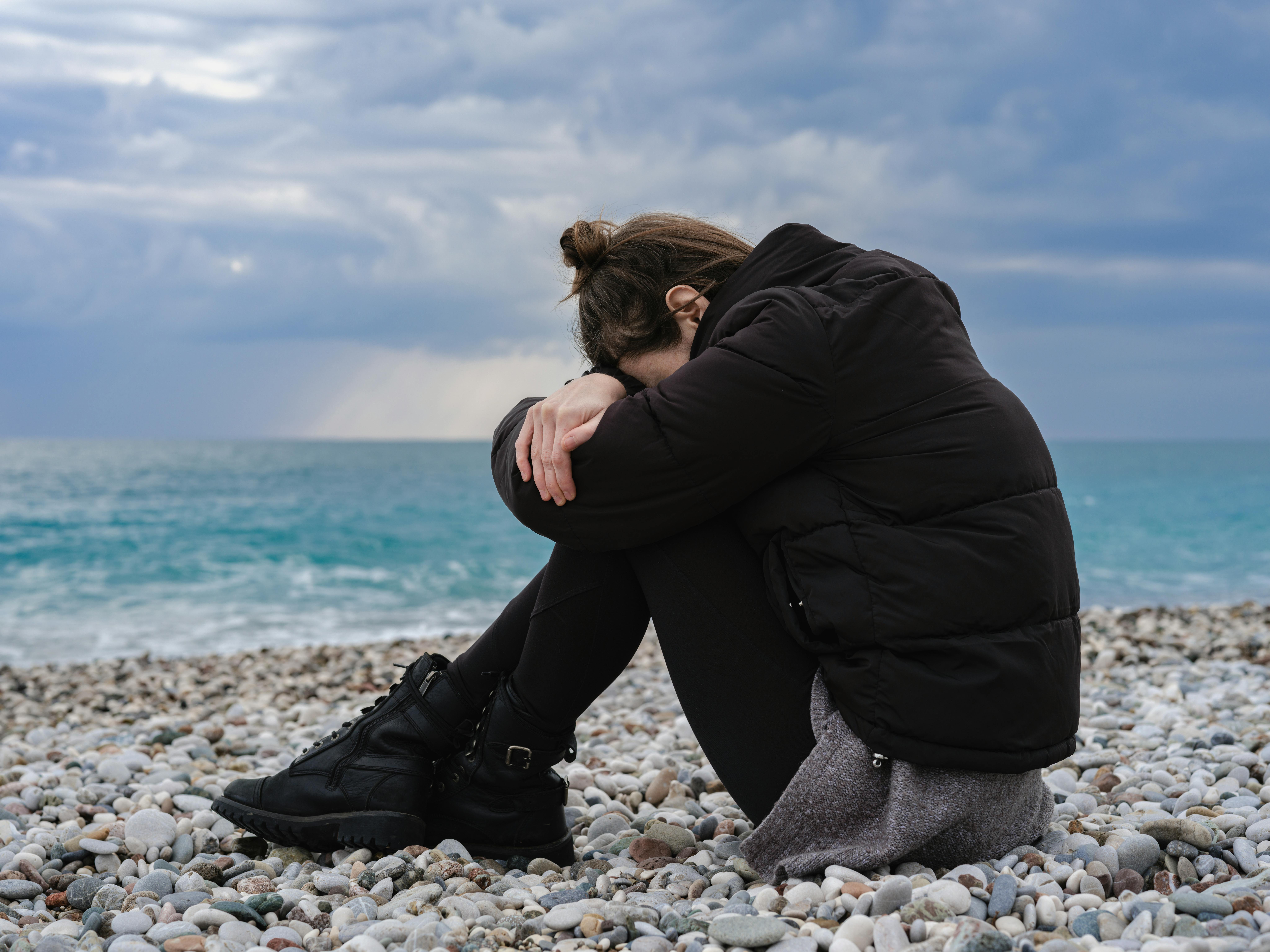 Woman wearing a jacket seated on a rocky shore