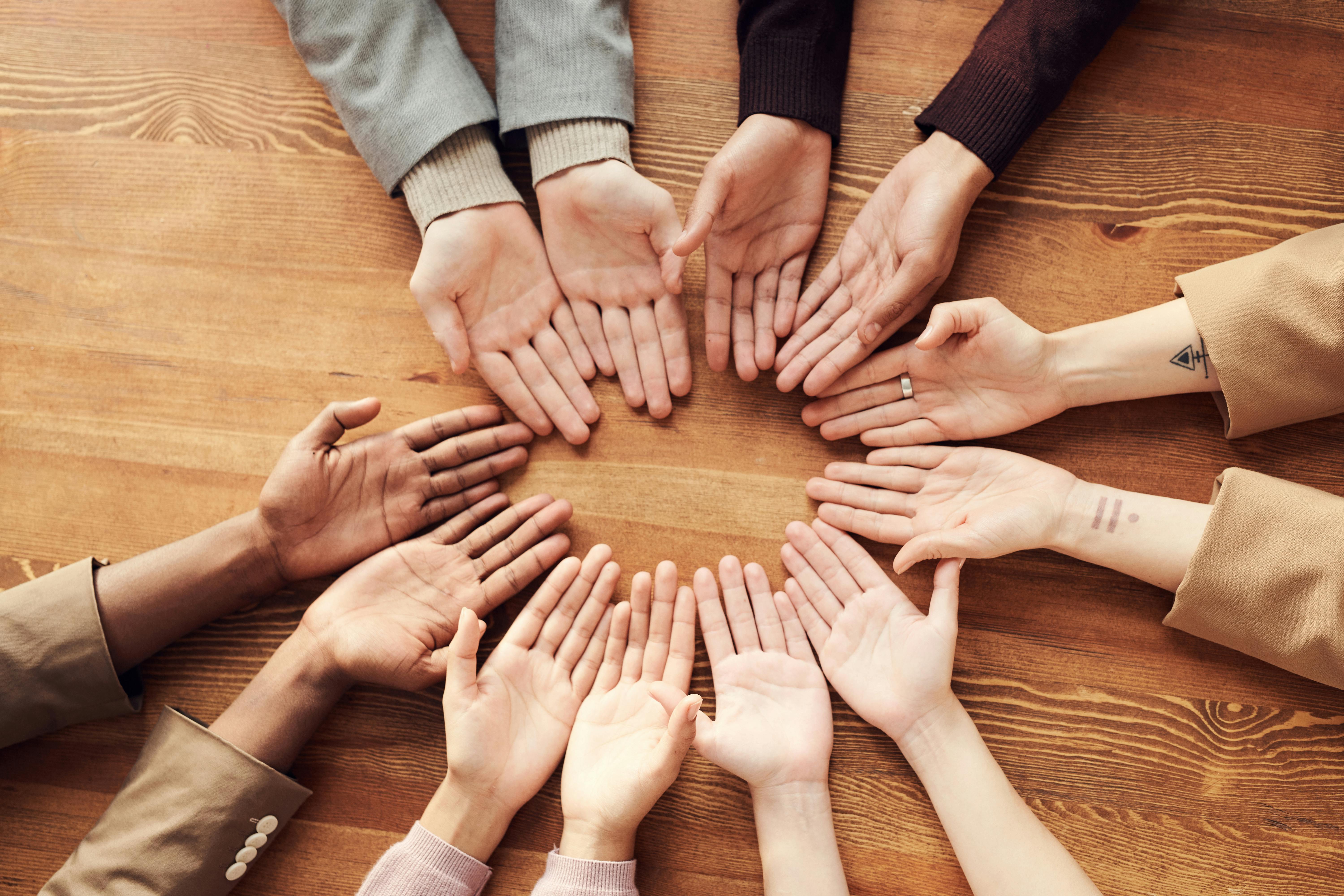 People forming a circle with their hands on a wooden table