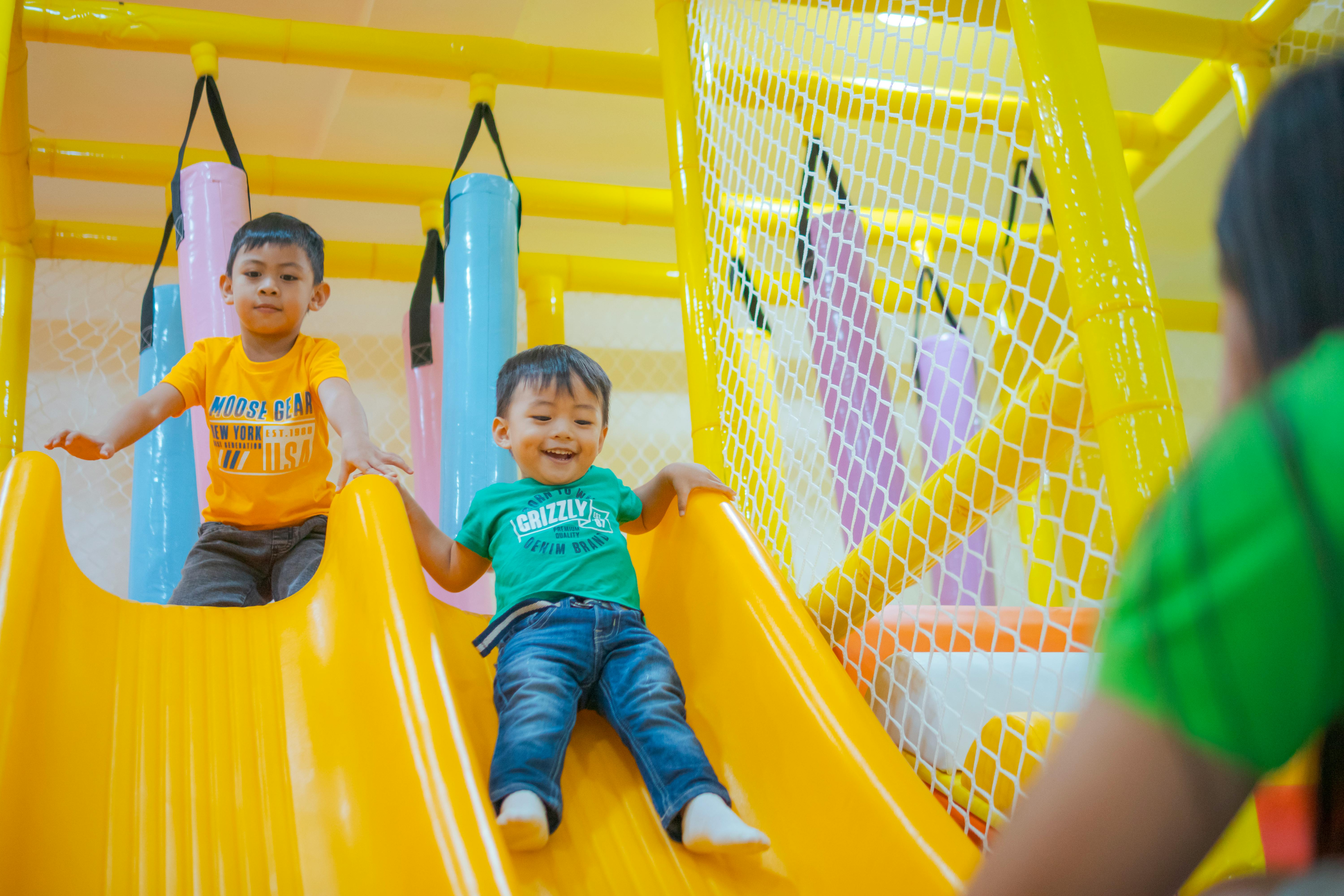 two young boys playing on a yellow slide at a playground