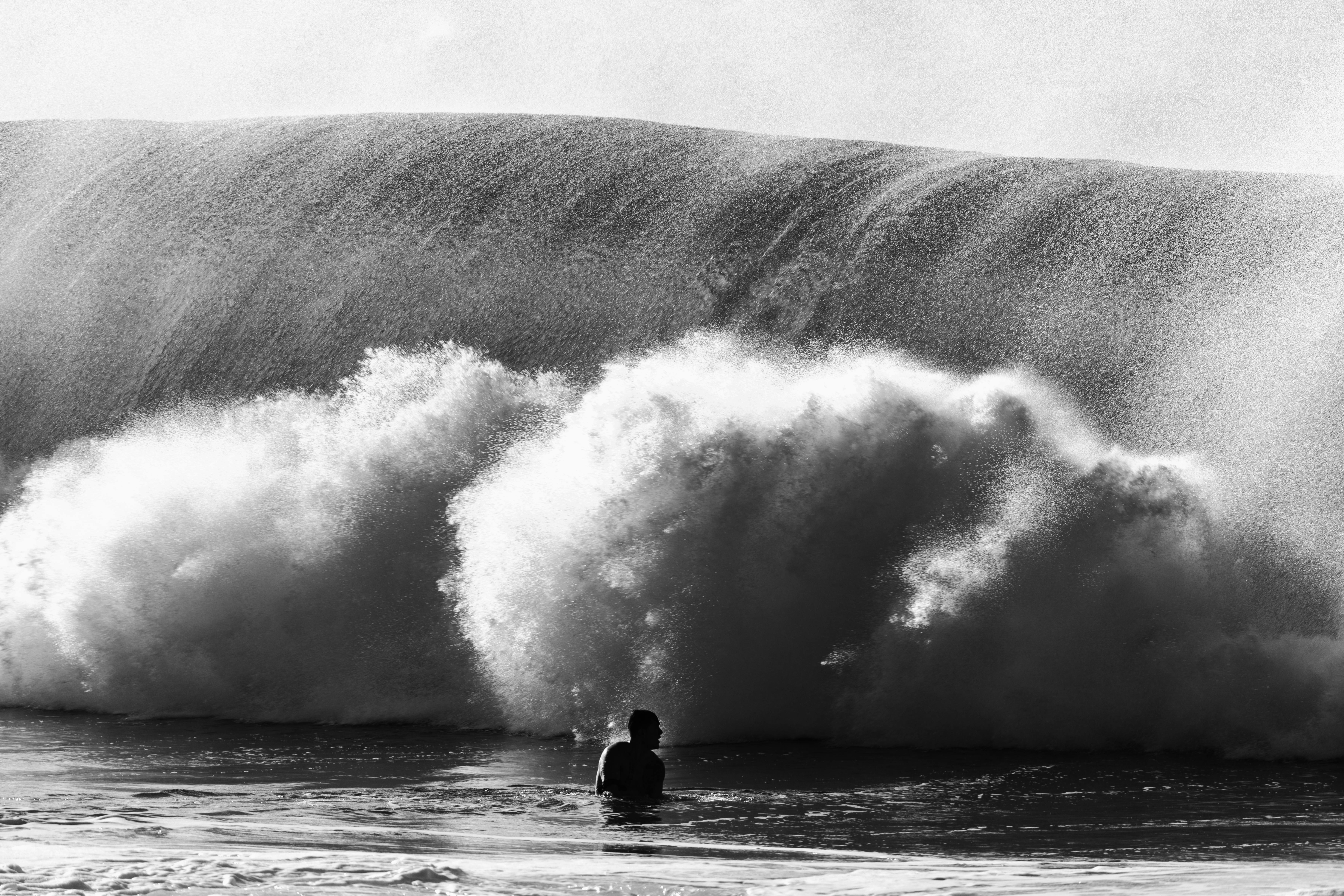 Silhouette of a person in the ocean standing in front of a large wave