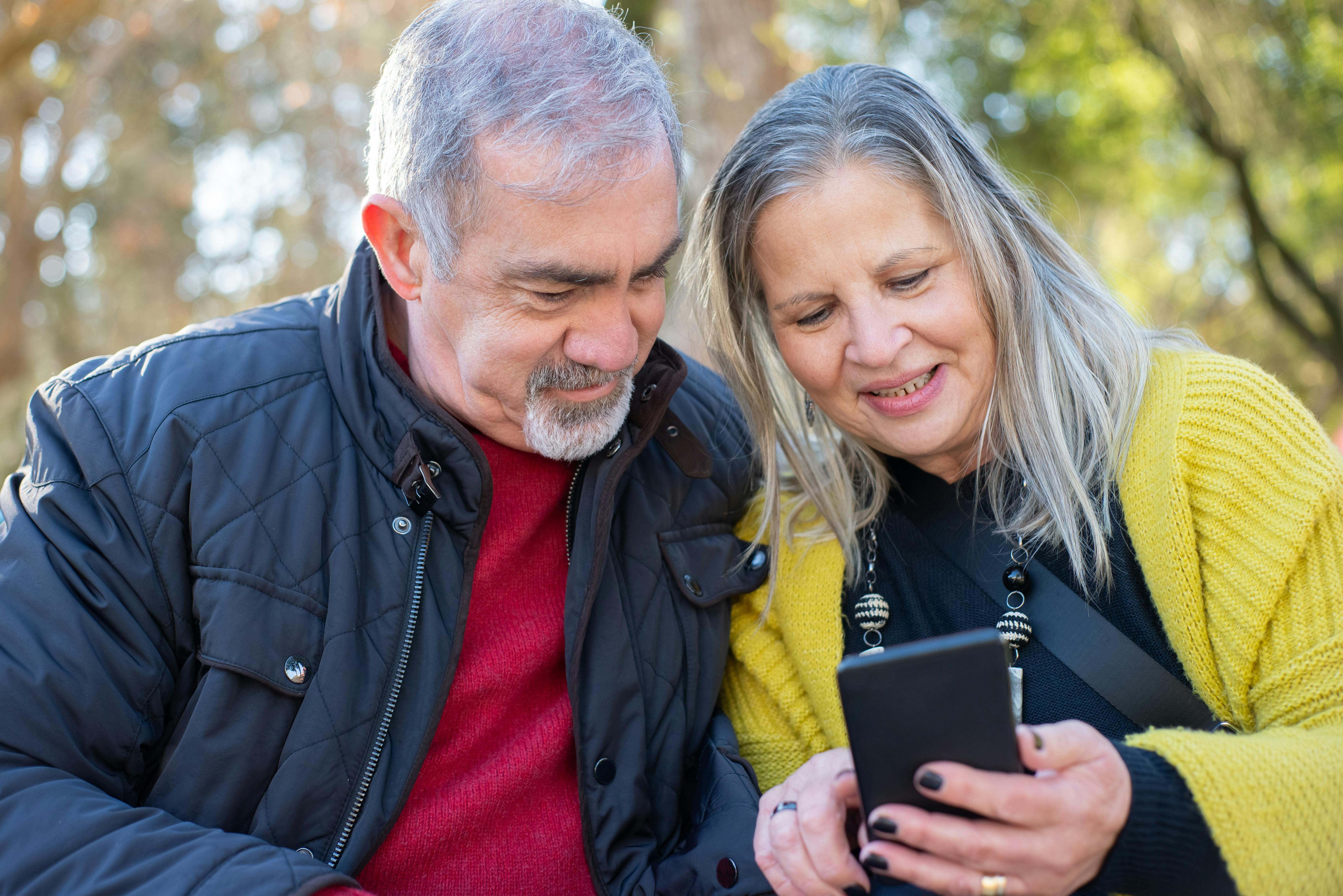 Two seniors standing outside looking at a phone together
