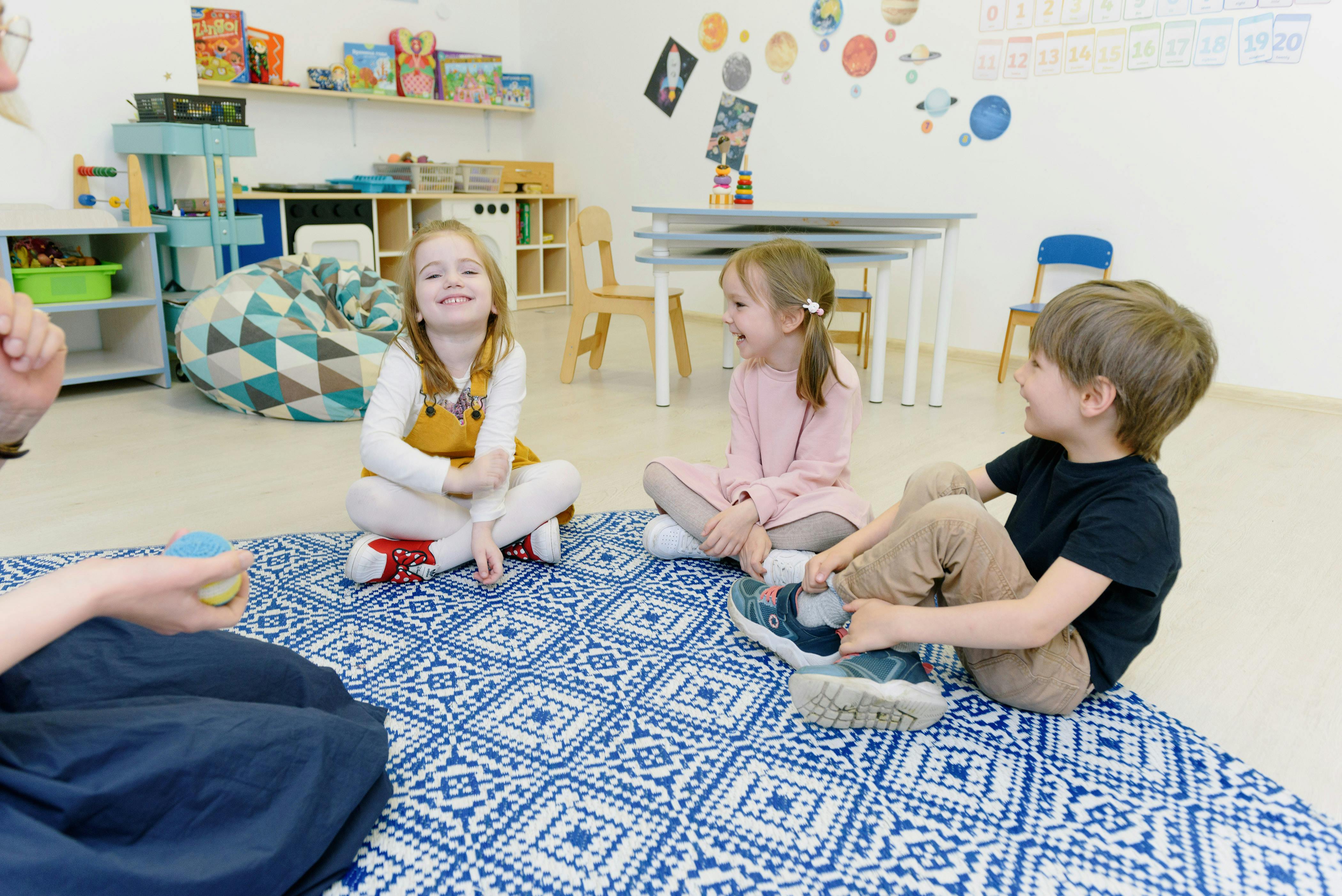 three children sitting on a rug in a classroom