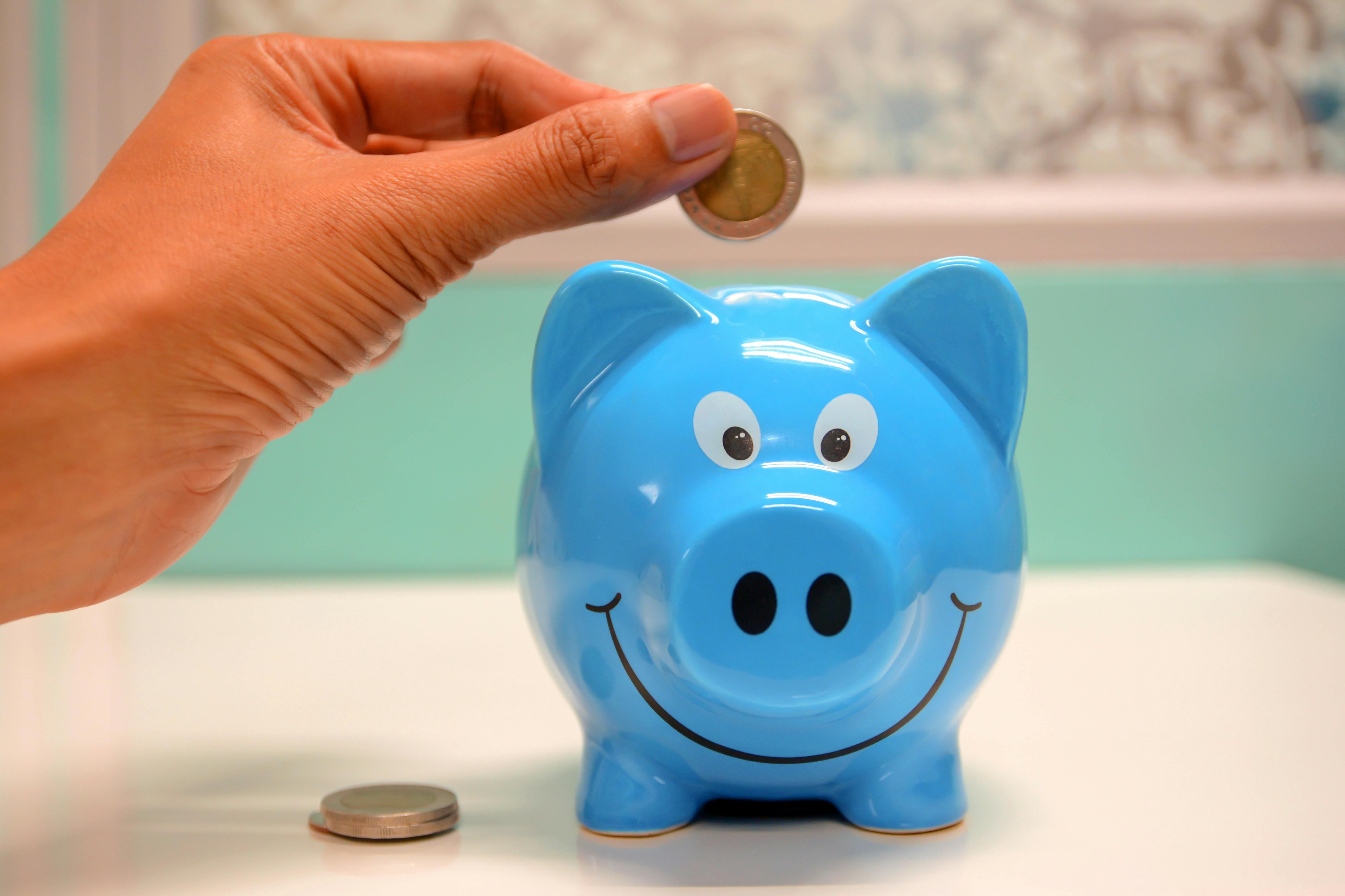 A person putting a coin in a blue piggy bank