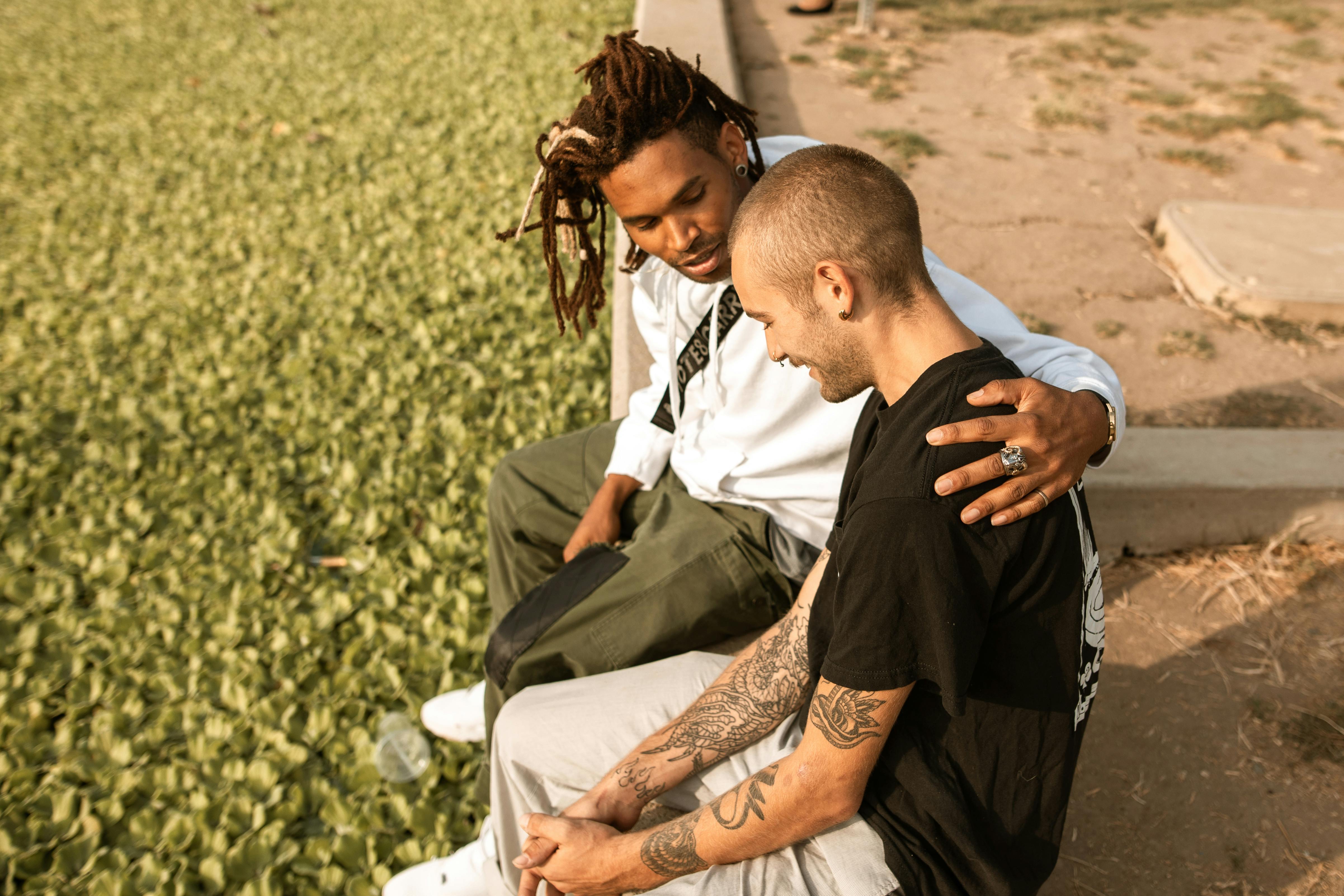 A man comforting a friend in a park 