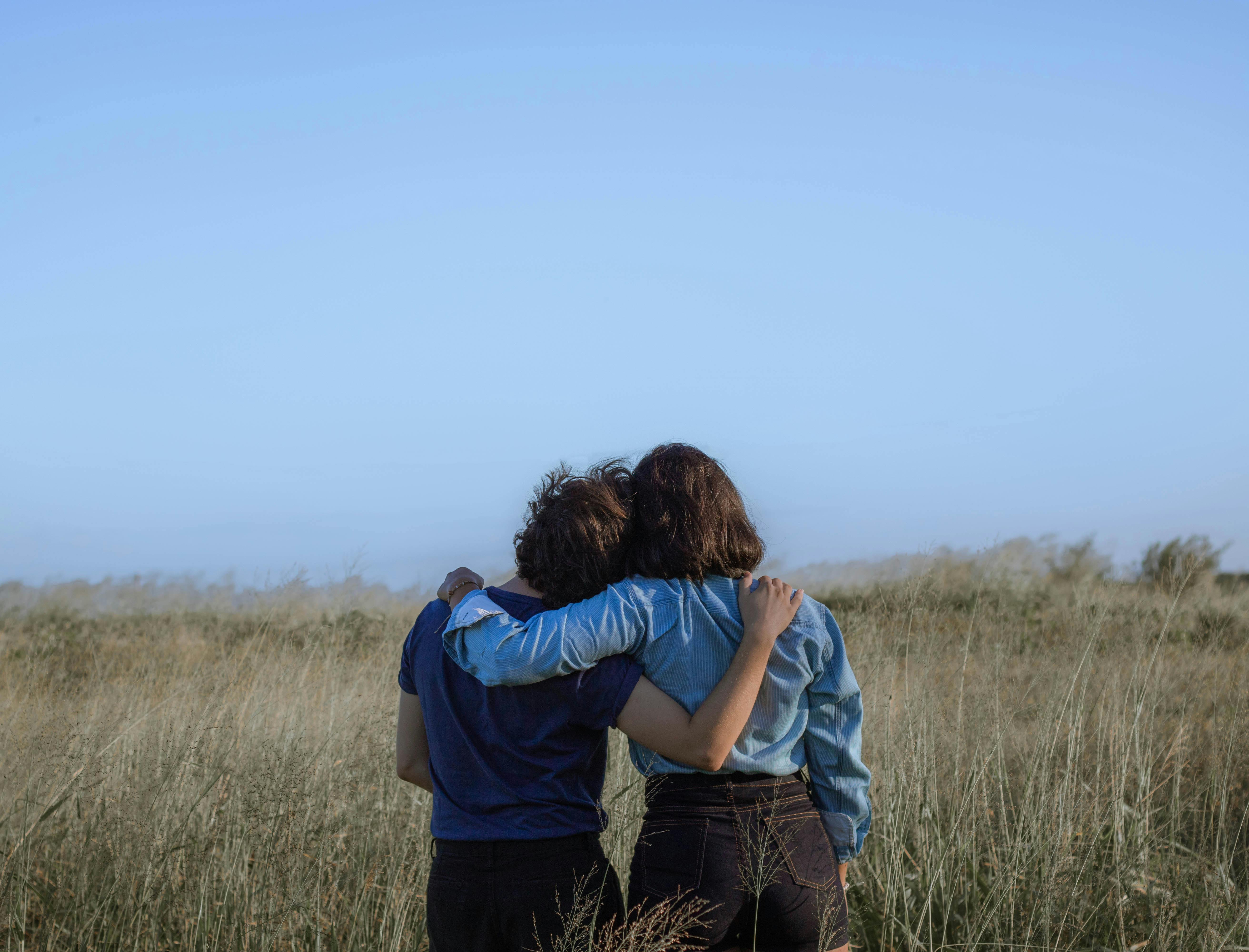 Two people leaning against each other in a meadow