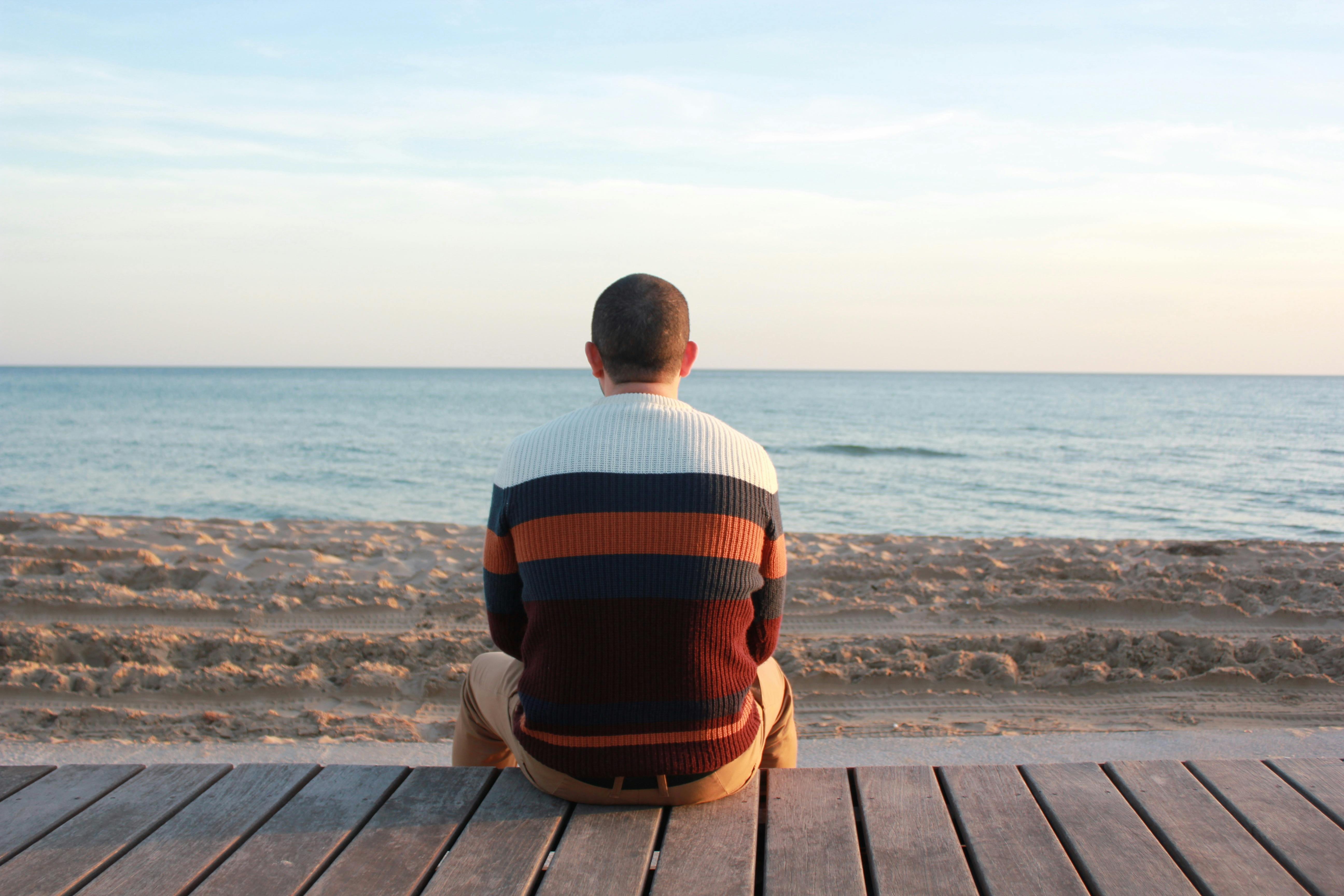 A man sitting on a boardwalk facing the ocean
