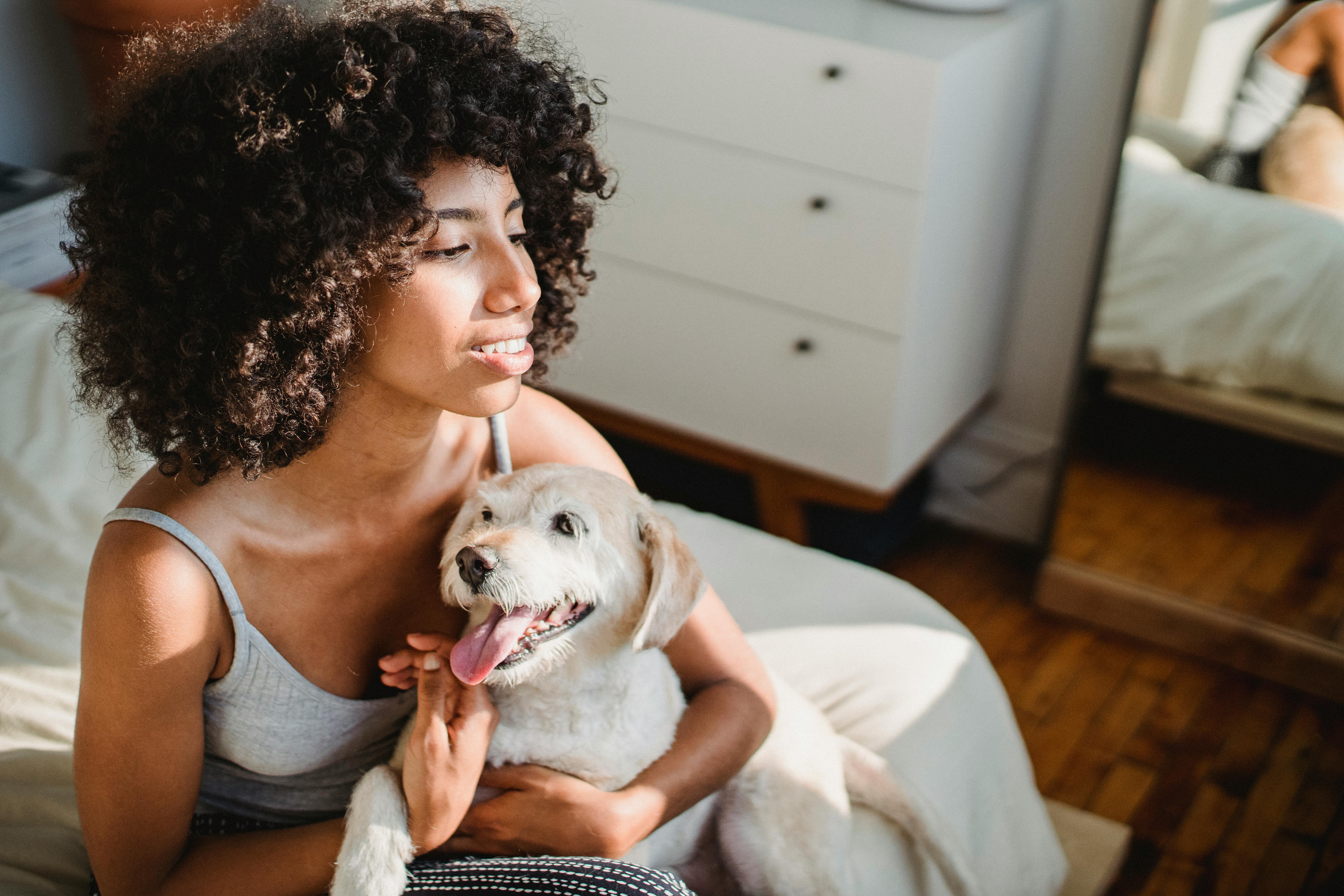 A black woman sitting on a bed at home and cuddling a puppy