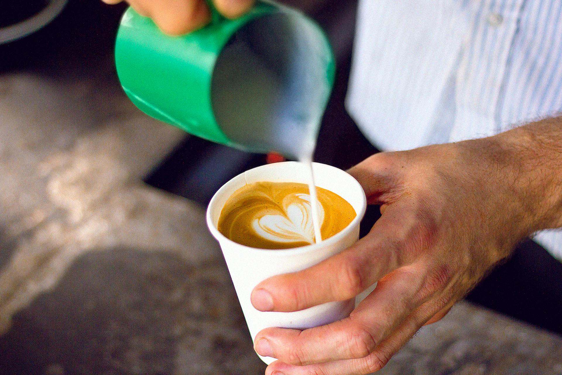 A person making a latte art heart in a cup of coffee