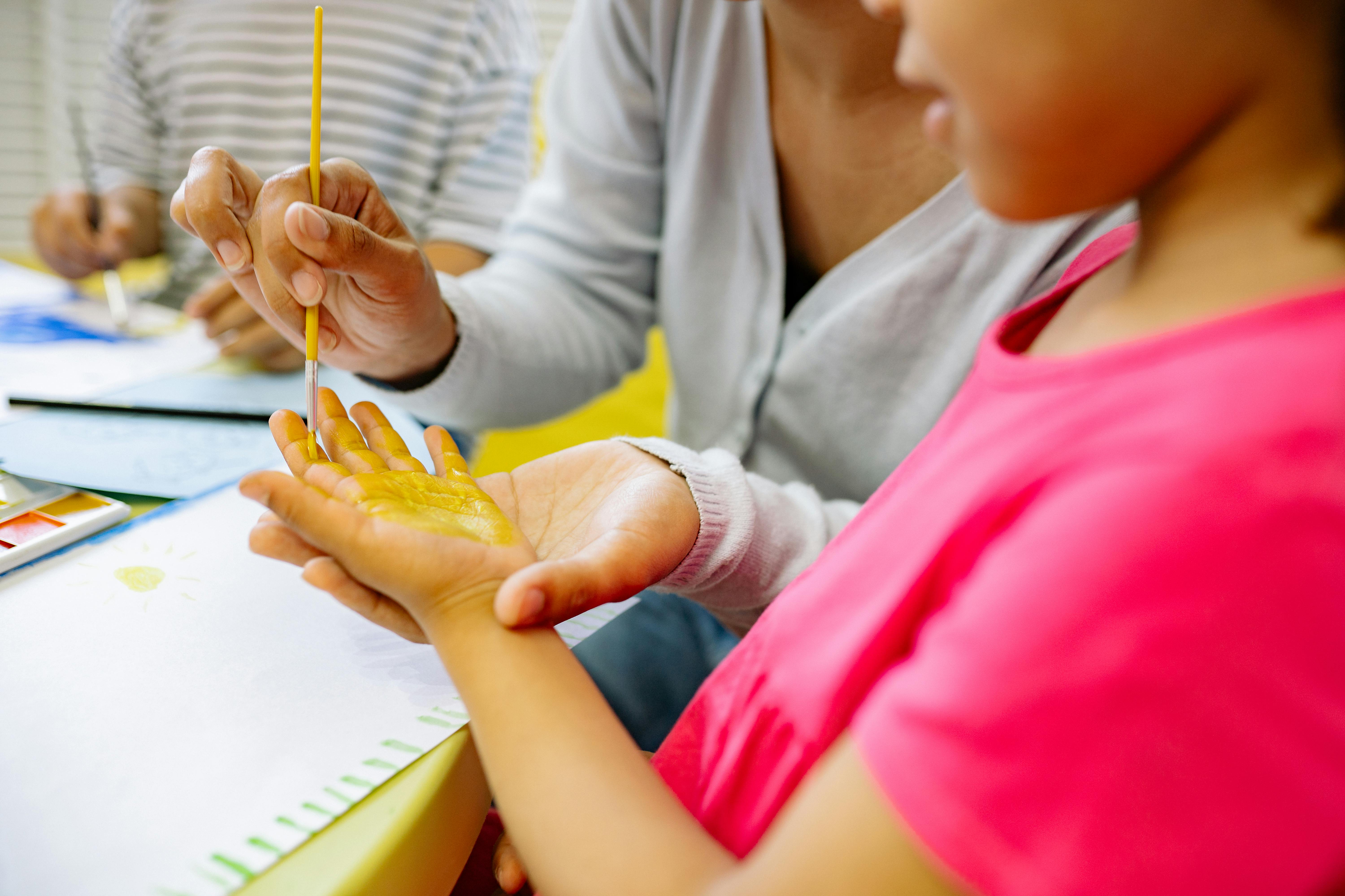 Person Painting A Girl's Hand With Yellow Color