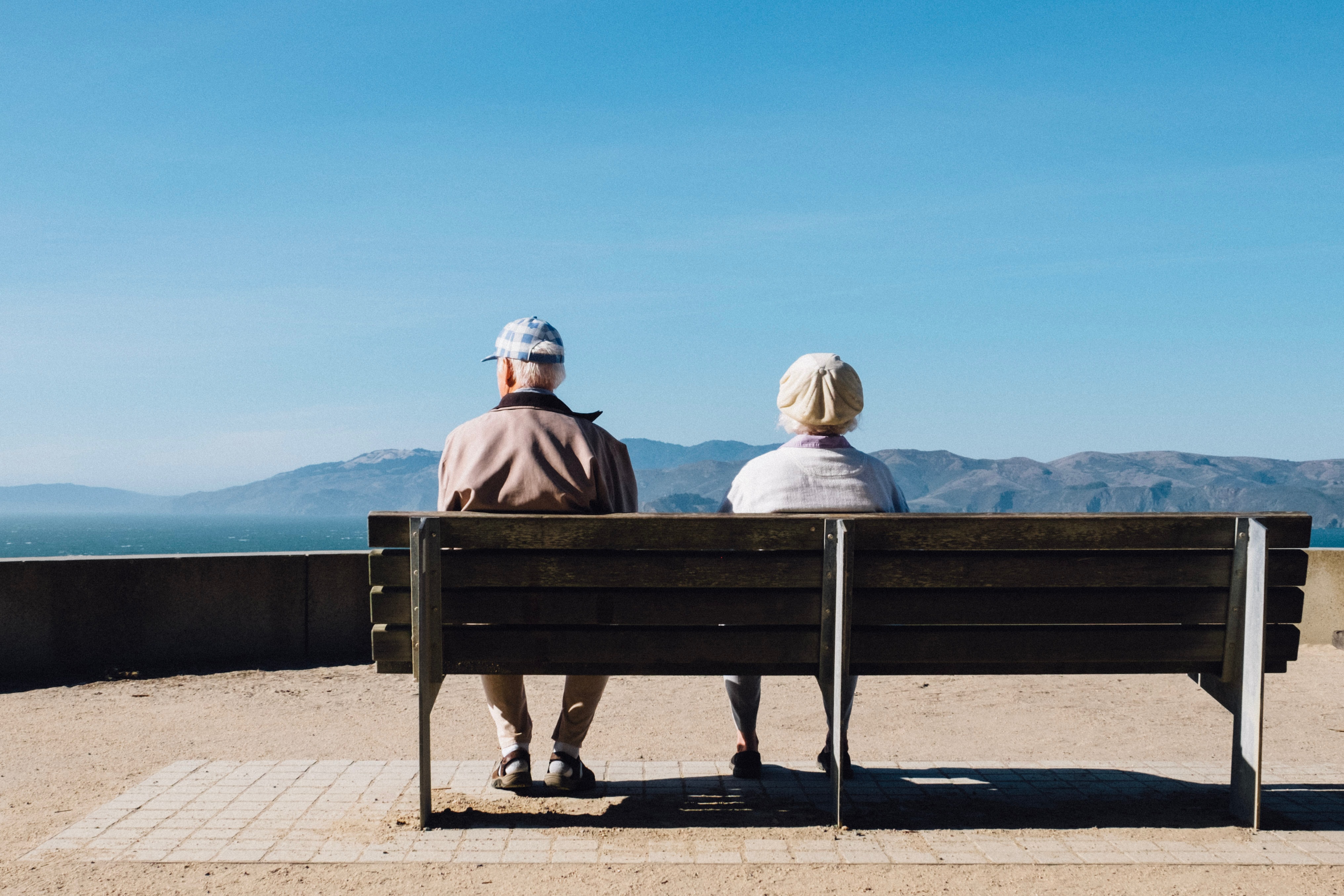 An elderly couple sitting on a bench facing sea