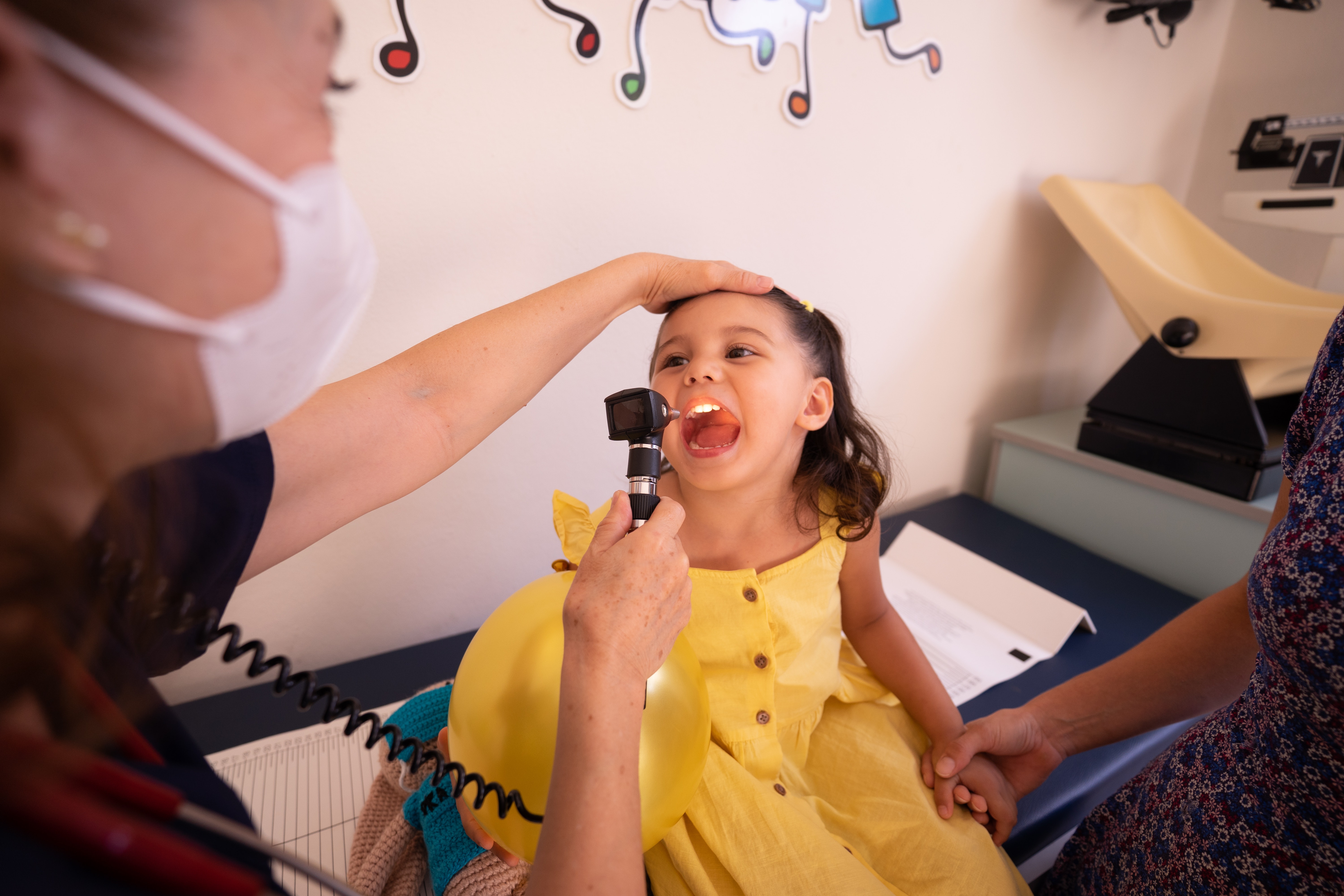A young girl in a yellow dress being examined by a doctor.